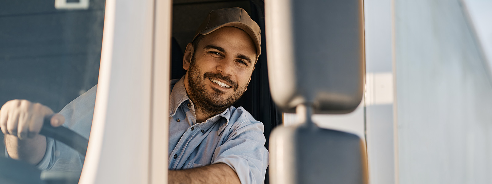 Happy professional truck driver driving his truck and looking at camera.