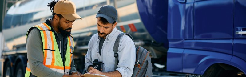 Dispatcher and truck driver going through shipment list on parking lot.