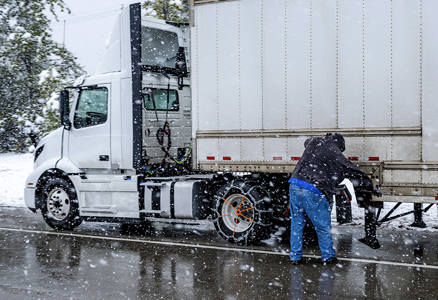 Truck driver puts chains on the wheels of the big rig semi truck with semi trailer to drive safely on a winter highway during a snow storm in the Lake Shasta region in California